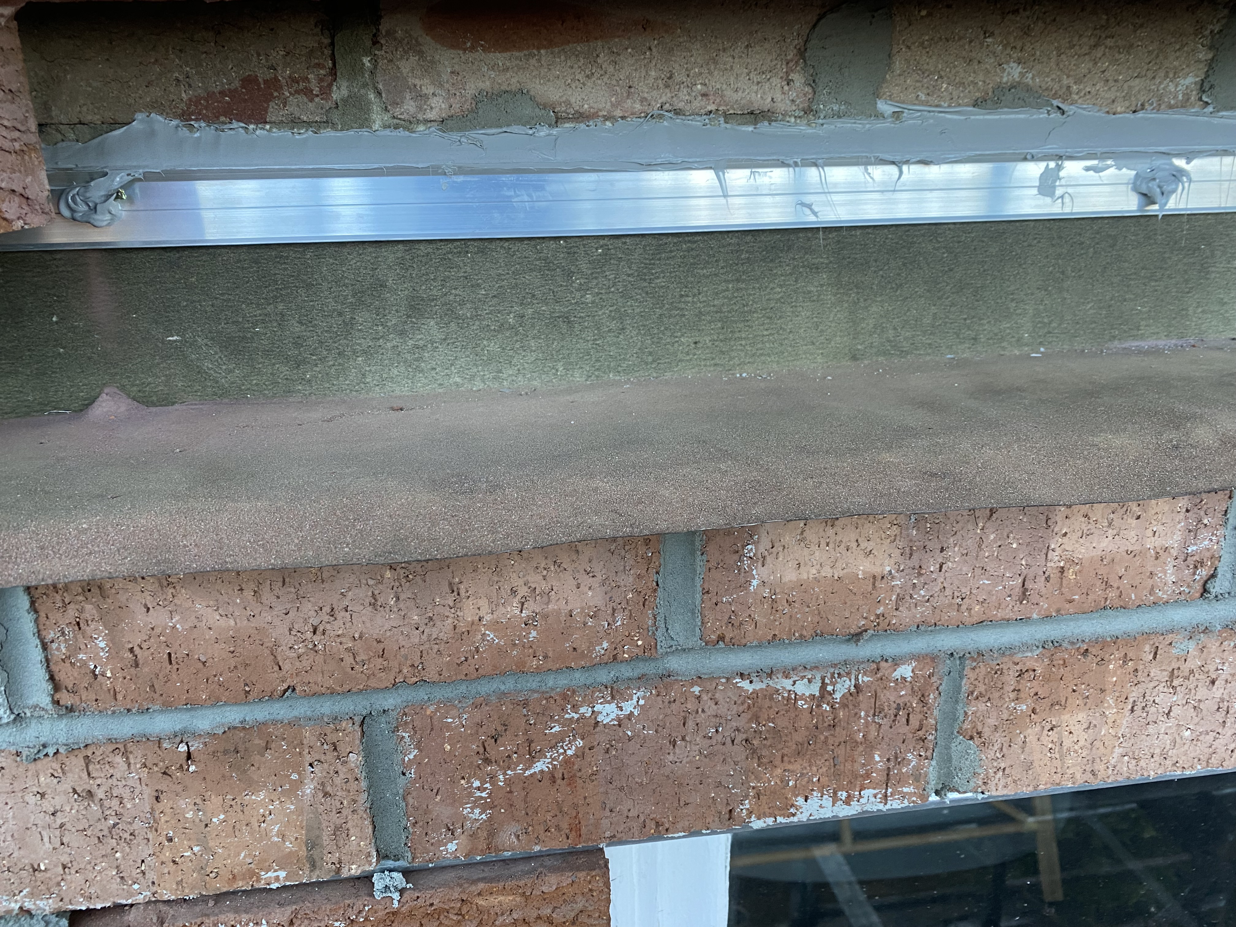 Newly installed galvanised steel lintel sitting above a sandstone sill with mortar bedding above