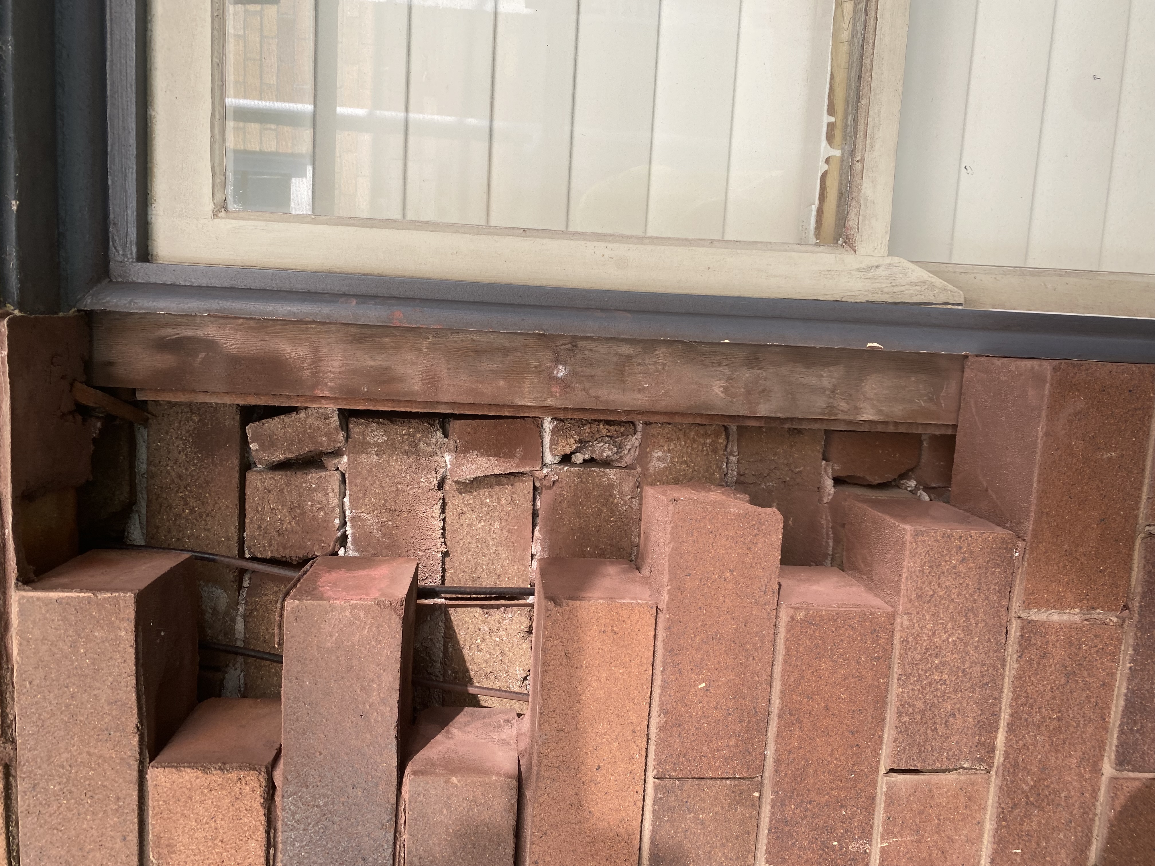 Closely-stacked spalled bricks below a window sill showing severe face fretting before remedial cut-out