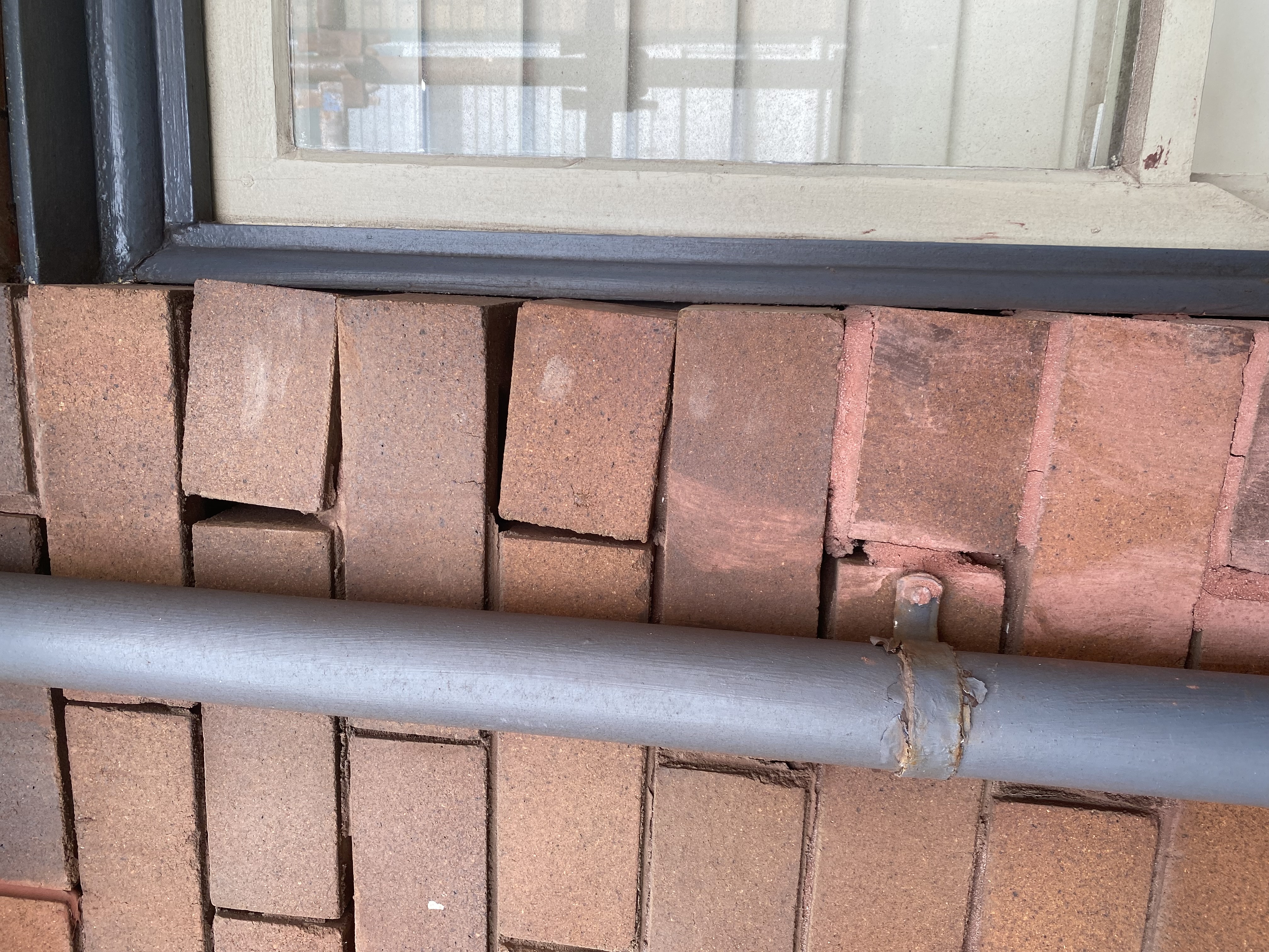Cracked and spalled bricks below a window sill with a steel handrail running across before repair