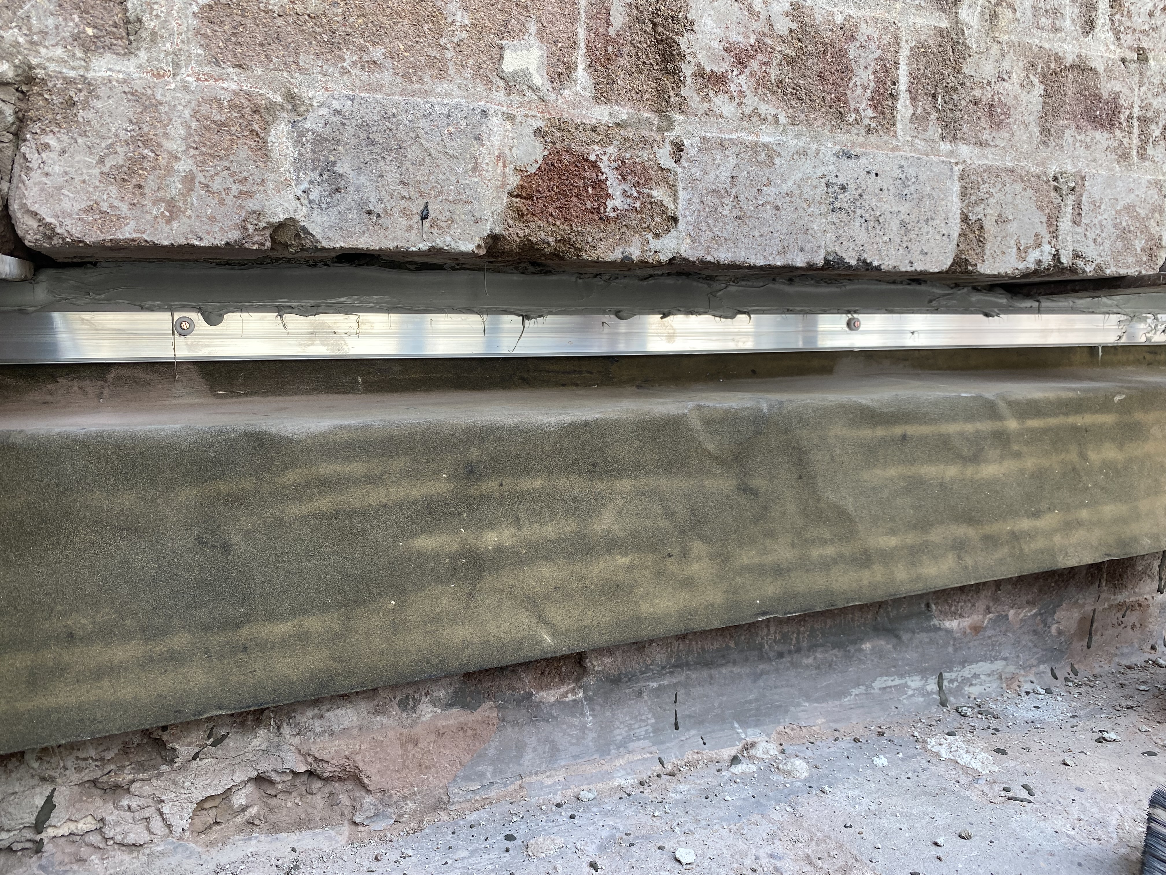 New stainless steel lintel bedded above a heritage sandstone sill on a red brick wall