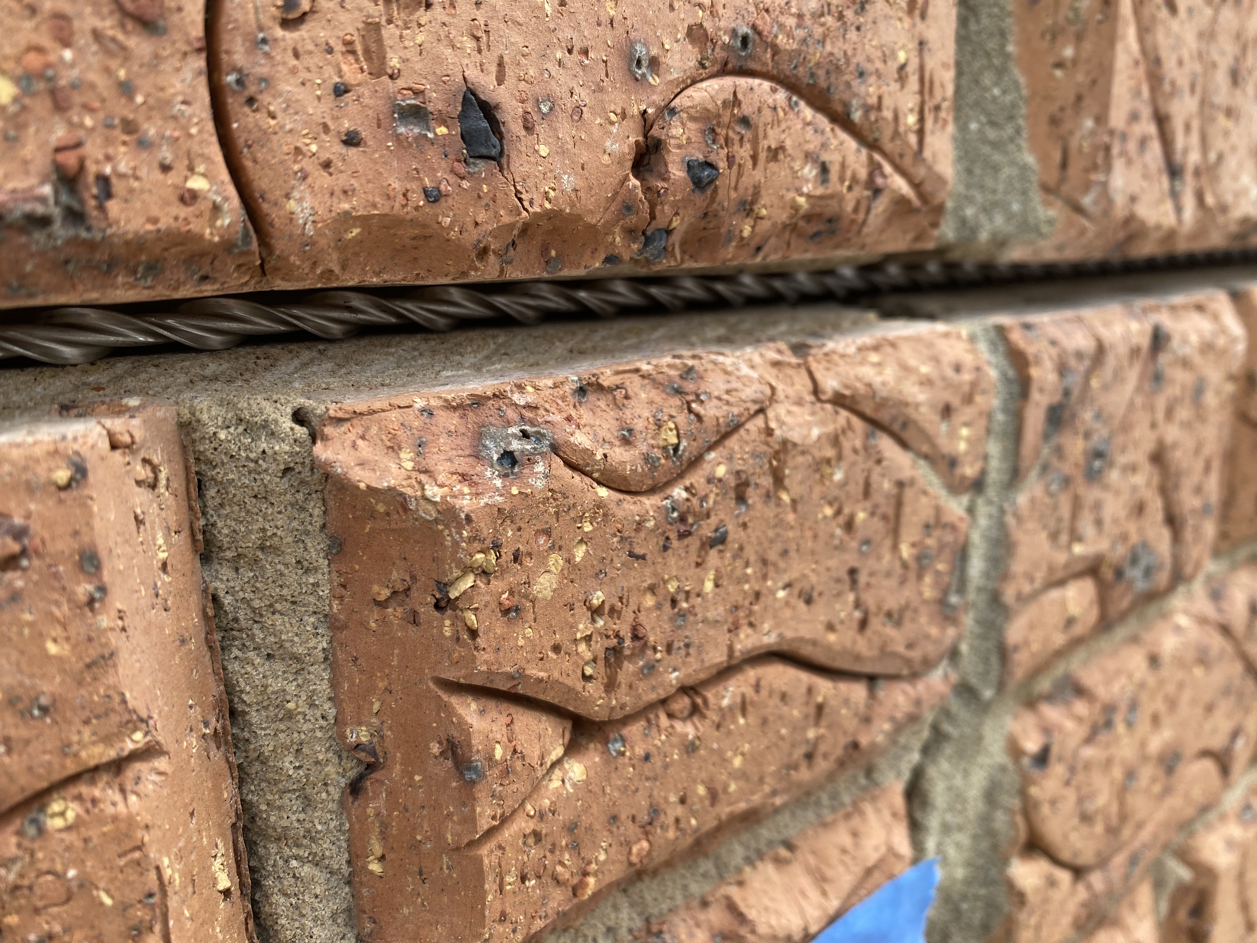 Close-up of a twisted helical stainless reinforcement bar set into a mortar slot between brick courses