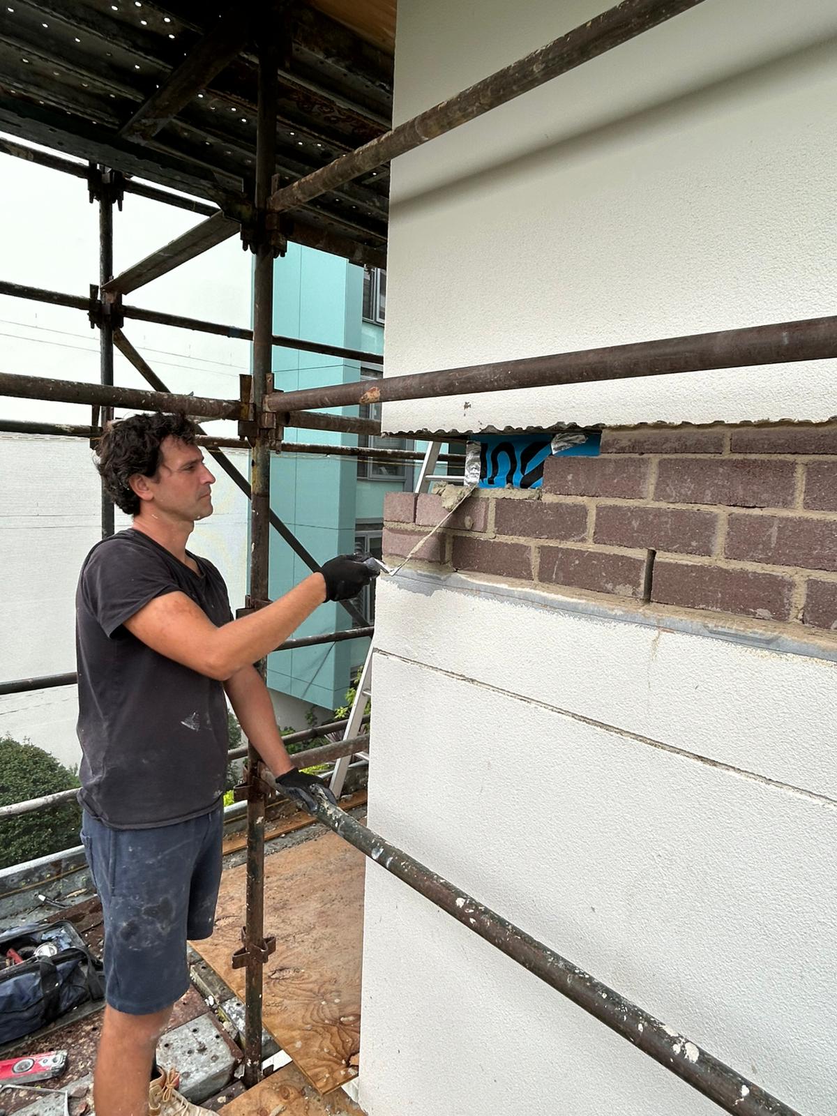 Working from scaffold on a brick course adjacent to a new cavity flashing line on the facade