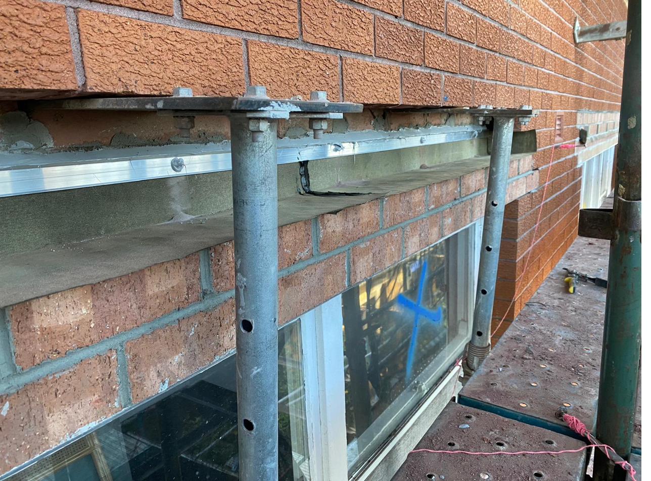 Acrow props with steel load-spreader plates holding brickwork above a new cavity flashing line during installation
