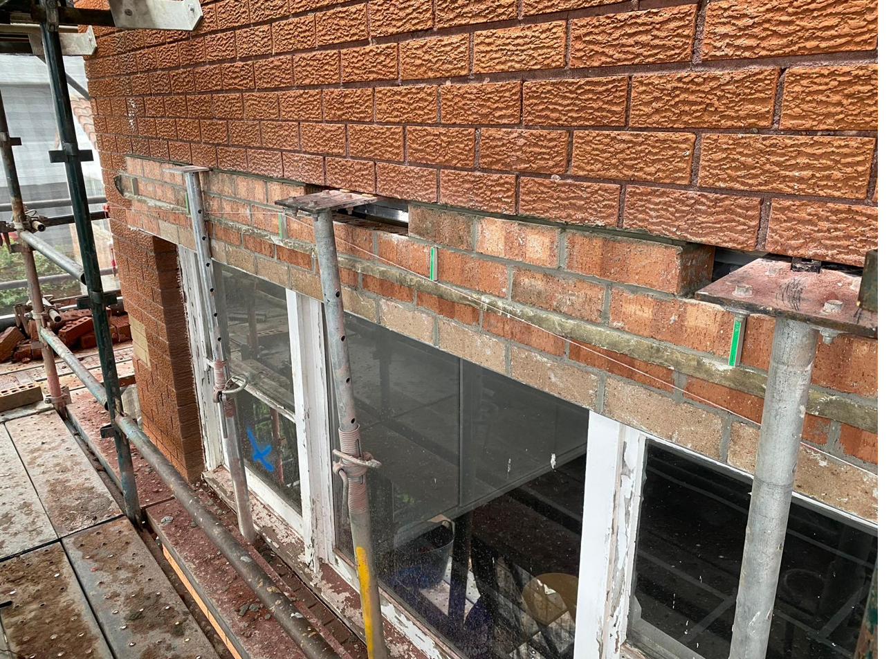 Lower brick course removed exposing new aluminium cavity flashing, acrow props holding the wall above