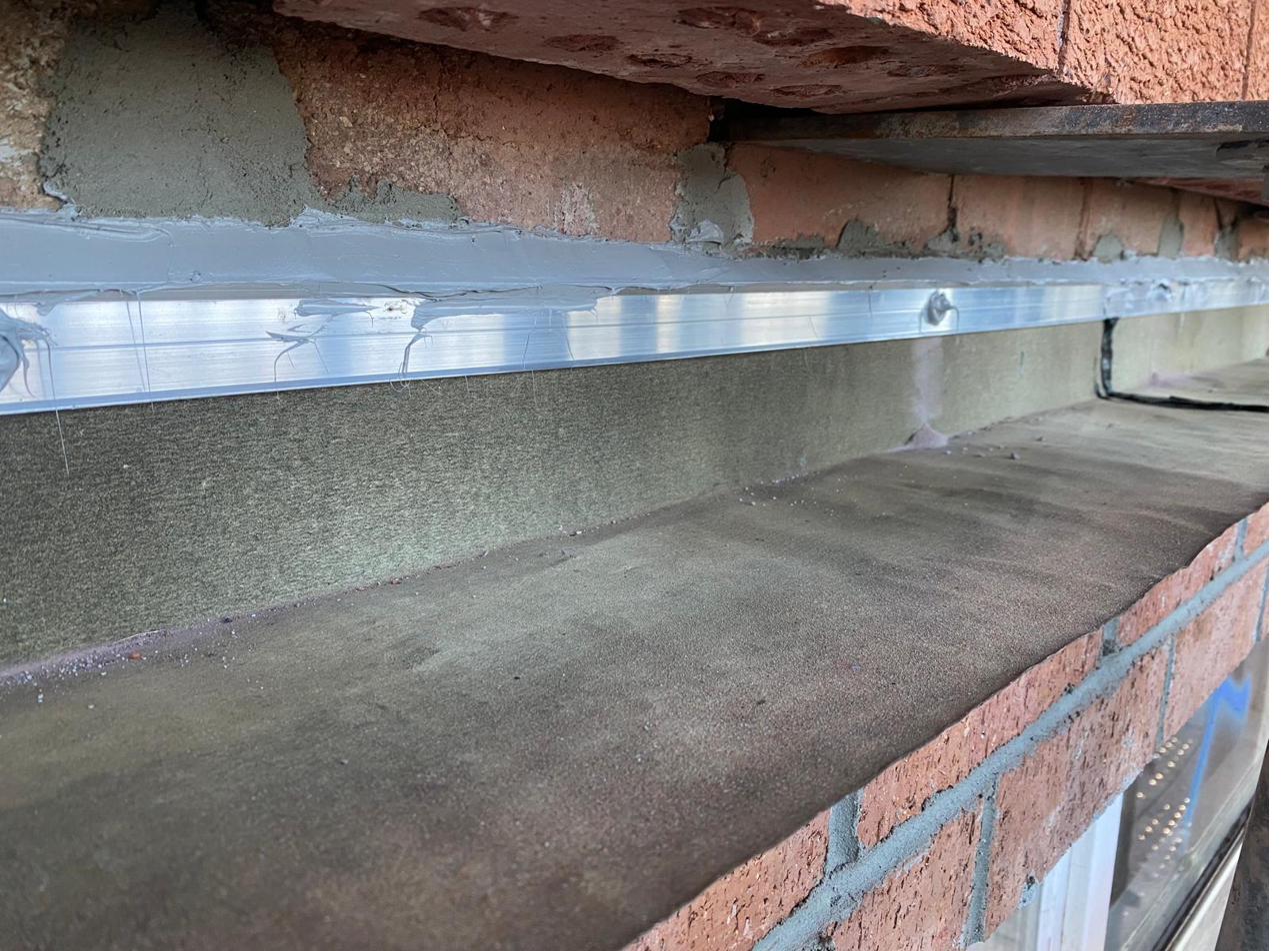 Angled detail of fresh aluminium cavity flashing dressed onto a sandstone sill above red brickwork