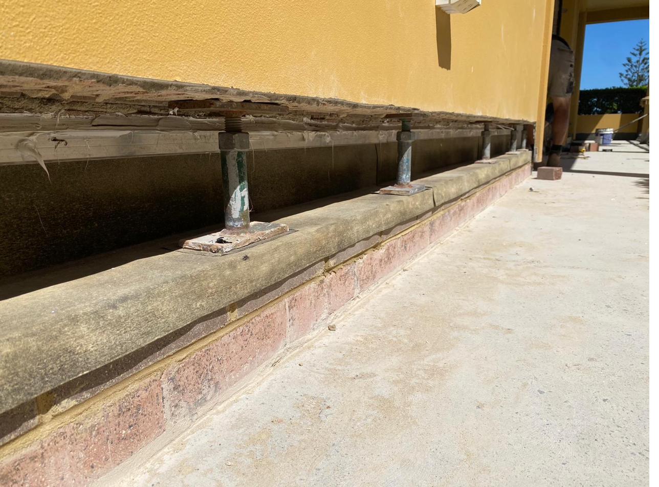 Concrete sill course propped on screw threads with cavity flashing space prepared below on a yellow rendered facade