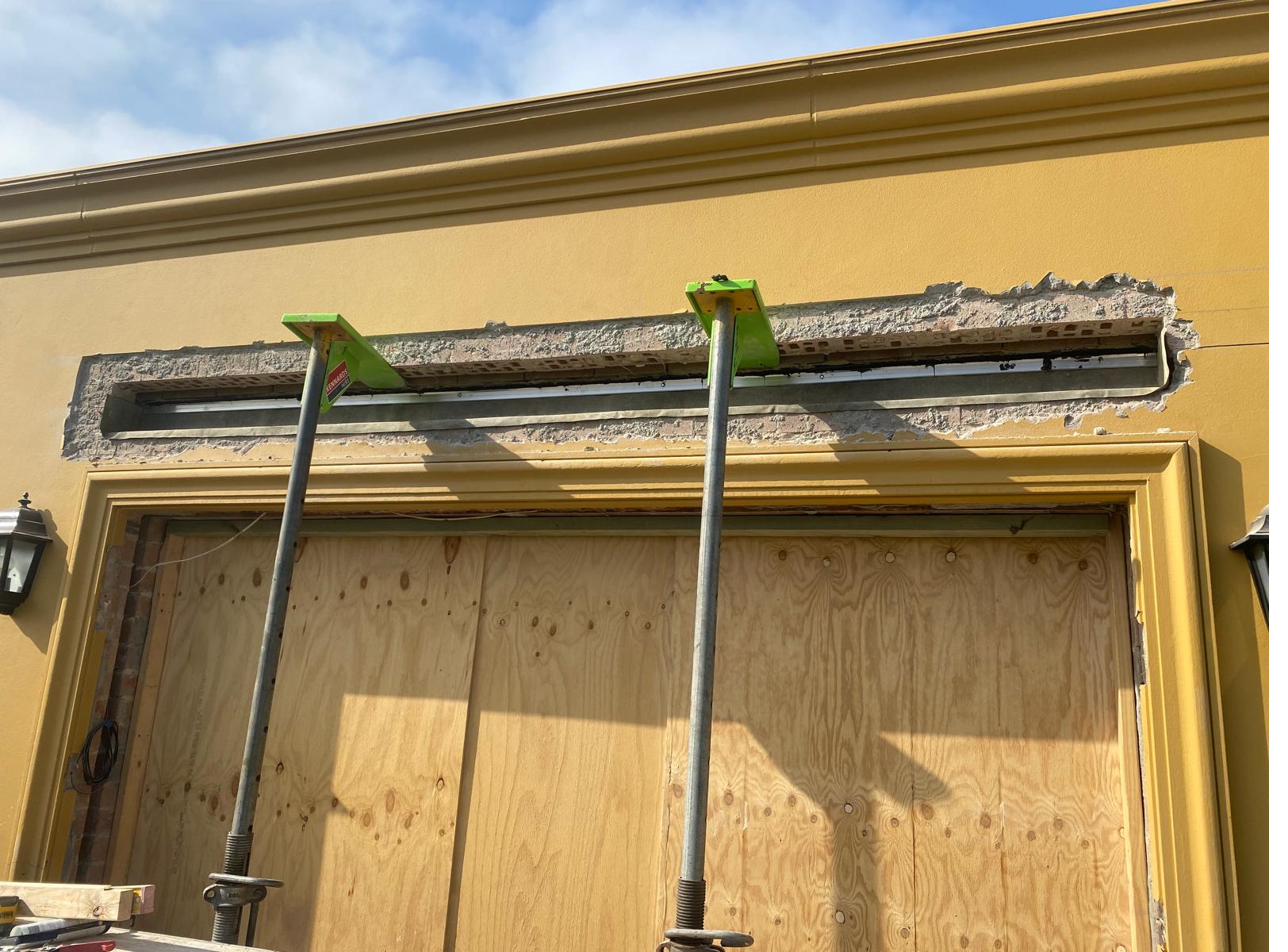 New aluminium cavity flashing installed above a doorway with green strongbacks and acrow props on a yellow rendered building